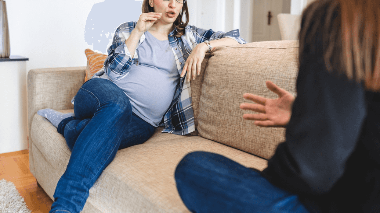 angry pregnant person seated on couch speaking to someone