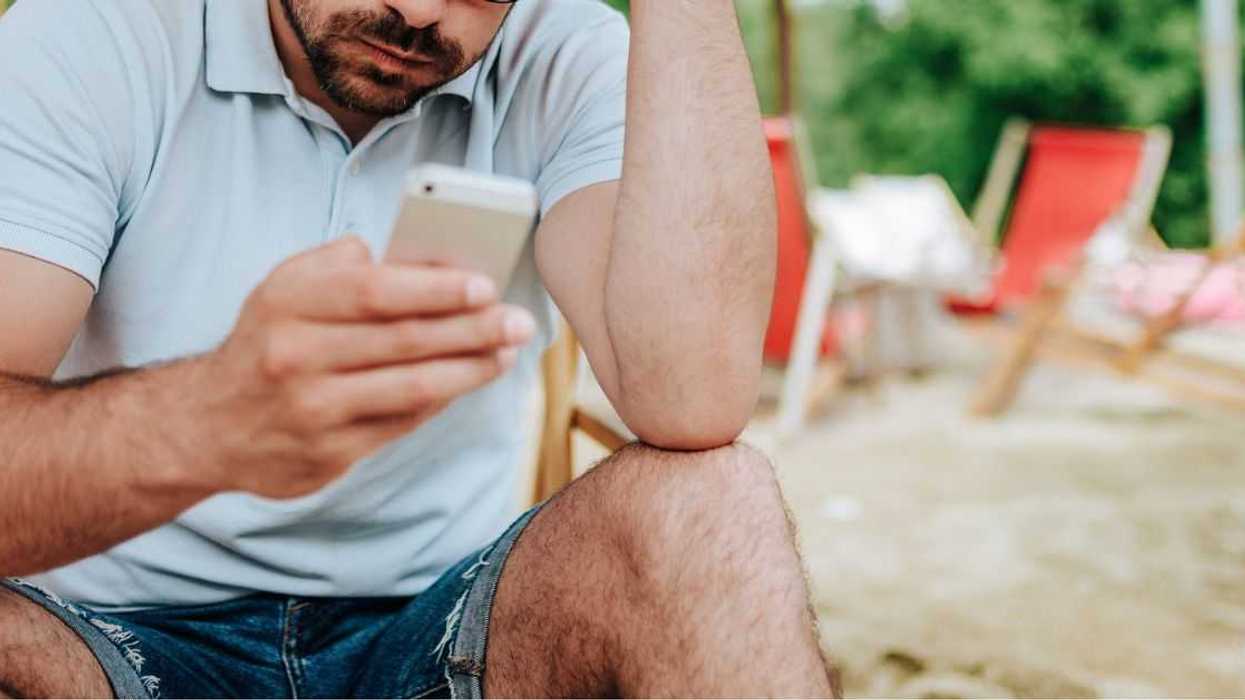 Annoyed man on the beach looking at a mobile screen.