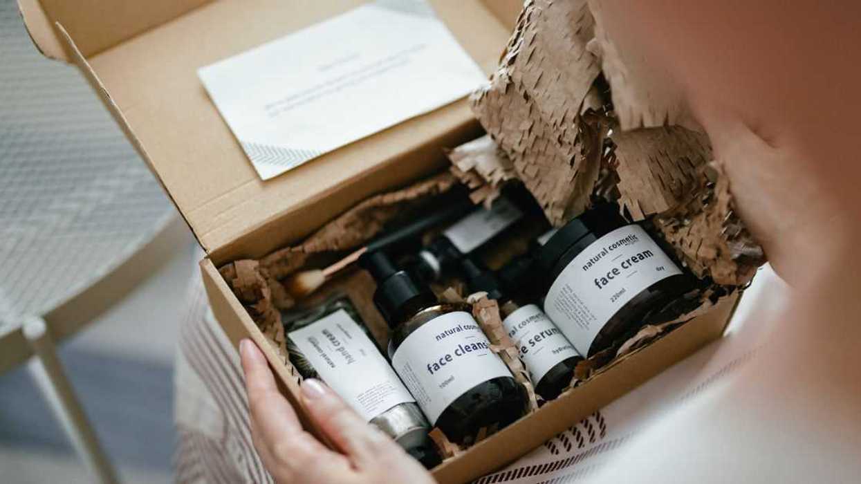 Anonymous woman holding a carton gift box on her knees. There are various natural beauty cosmetics products inside and a personal paper note.