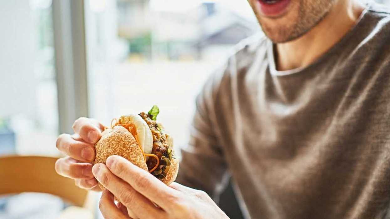 Asian man eating a veggie burger at a vegan cafe.