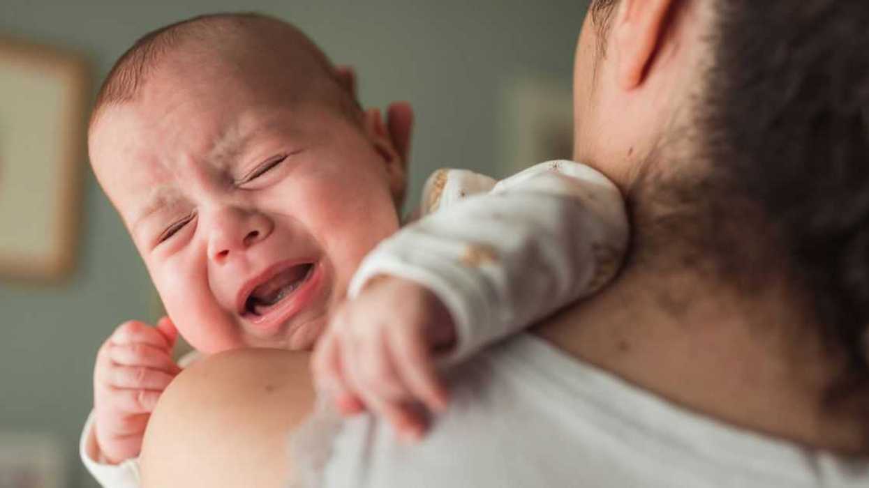 Baby with eyes closed screaming and crying on their mother's shoulder.