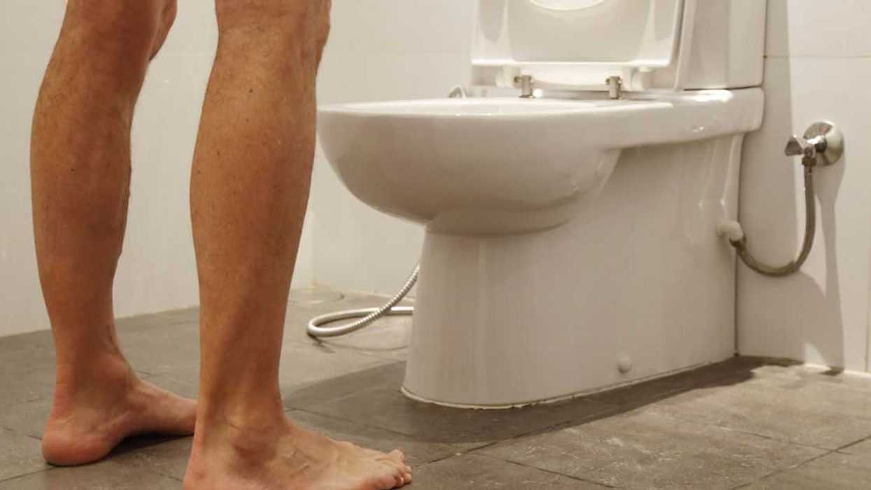 Back shot of a man's feet standing over a toilet.