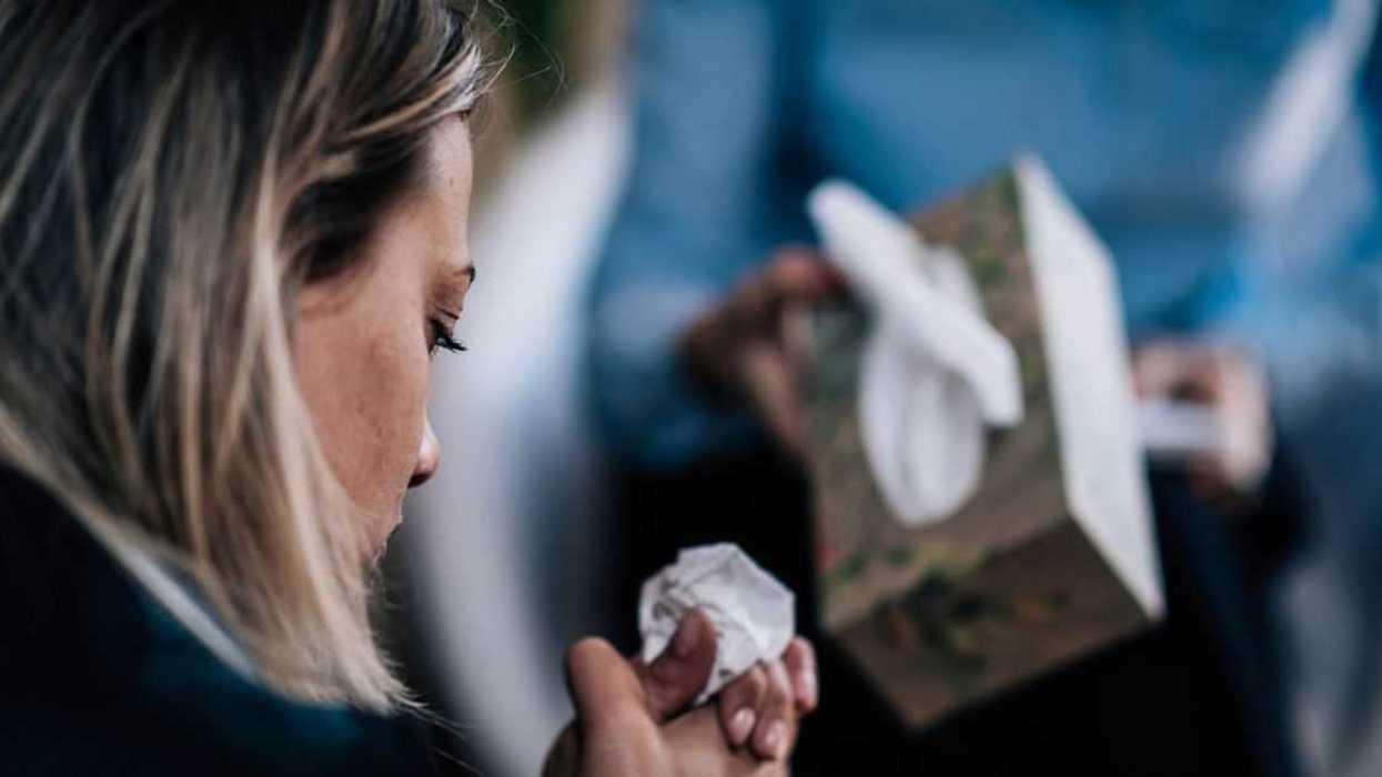 Back shot of a troubled woman crying, talking about her problems. A person in the background offers her tissues.