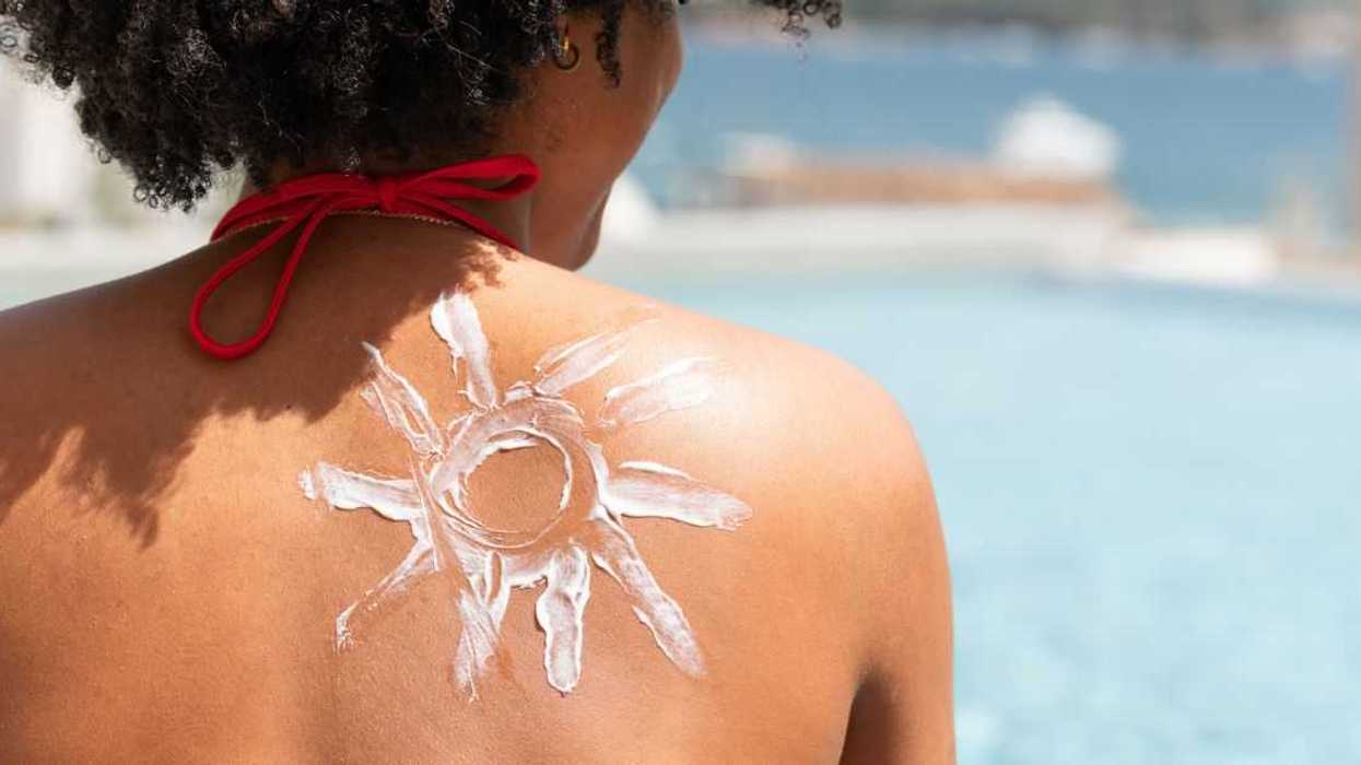 Back shot of a woman sitting on the beach with a sun made of sunscreen on her back.