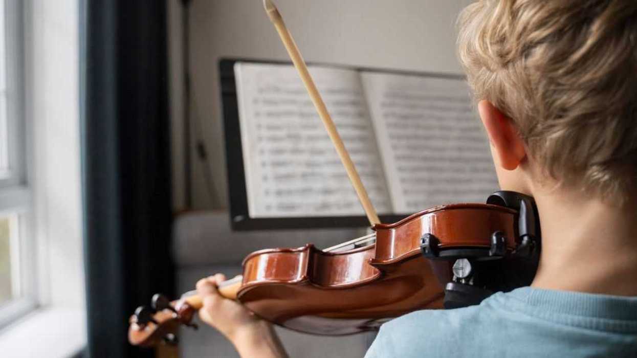 Back shot of boy practicing violin with sheet music at home.