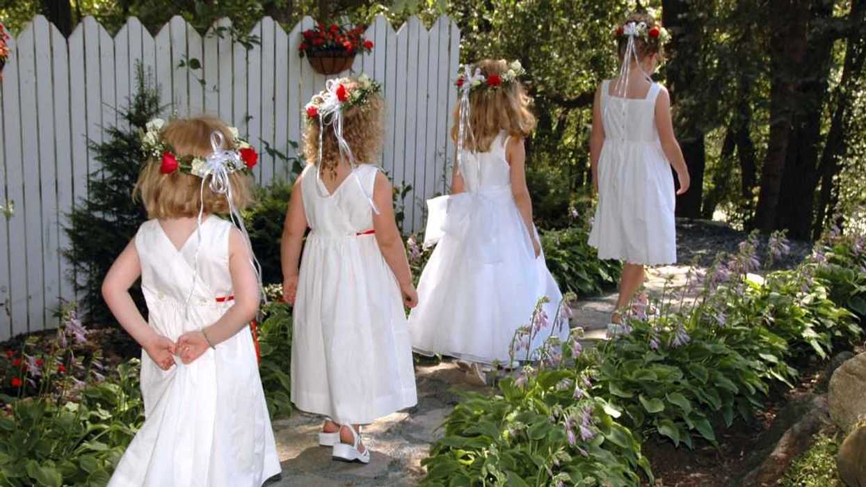 Back shot of four little flower girls walking through the garden.