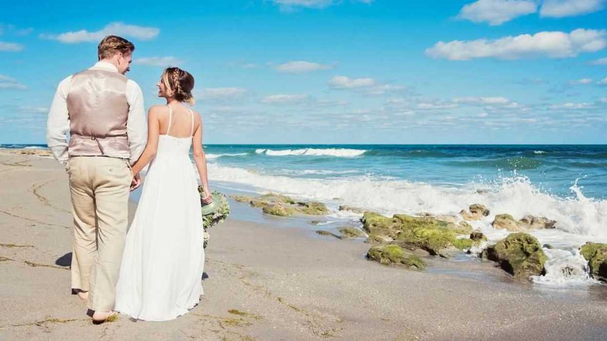 Back shot of newlyweds walking on the beach.