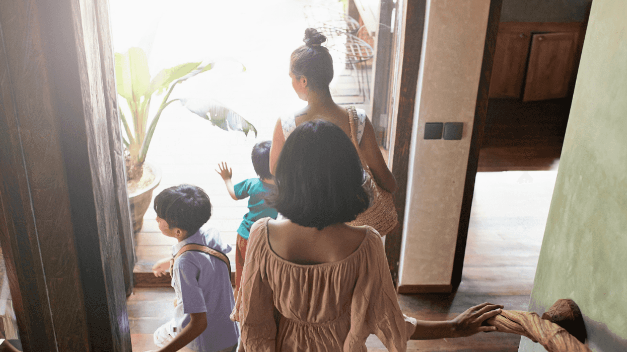 Back shot of two women with children leaving a house.