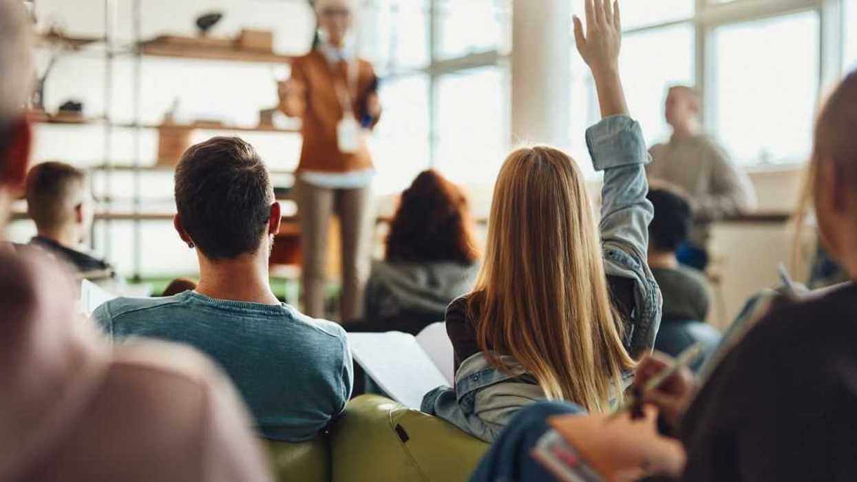 Back view of female student raising her hand to ask a question while having a class in a casual classroom.