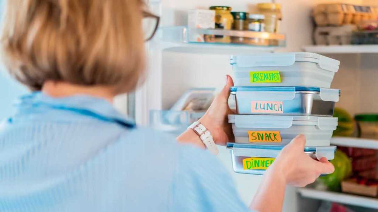 Back view shot of a woman taking or putting lunch boxes cooked in advance, ready to be served into fridge. Containers with eco healthy food. Pre-cooking concept.