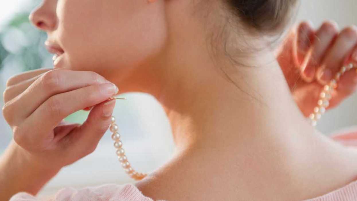 BAckshot of a woman putting on pearl necklace.