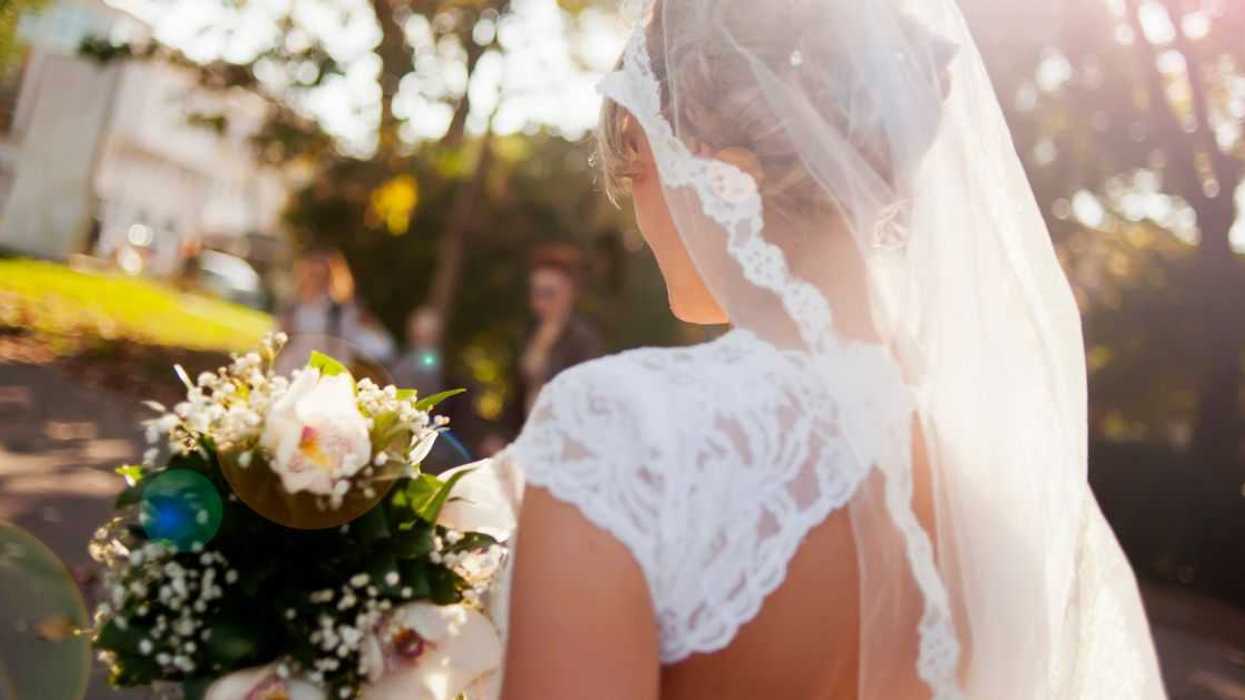 Beautiful bride holding flower bouquet view from back, lens flare.