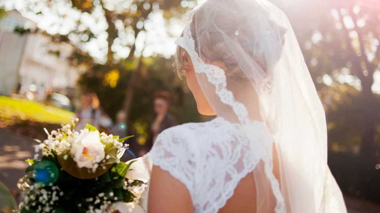 Beautiful bride holding flower bouquet view from back, lens flare.