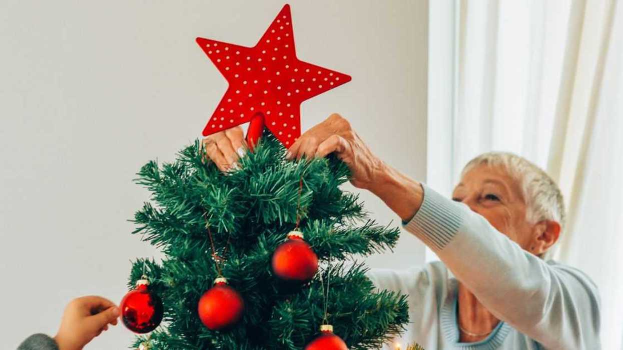 Beautiful senior woman putting the Christmas star on top of the Christmas tree.
