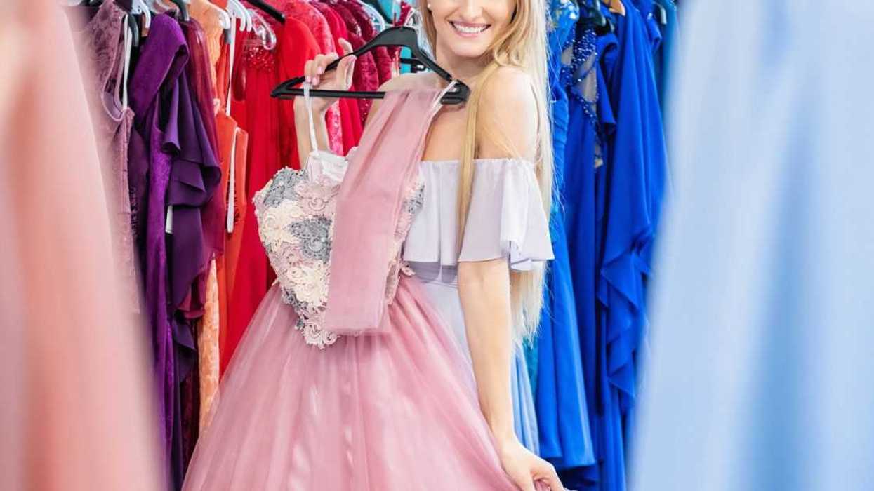 Beautiful woman shopping and choosing the right dress for luxury event. Young woman holding and trying on elegant gown and smiling at camera.