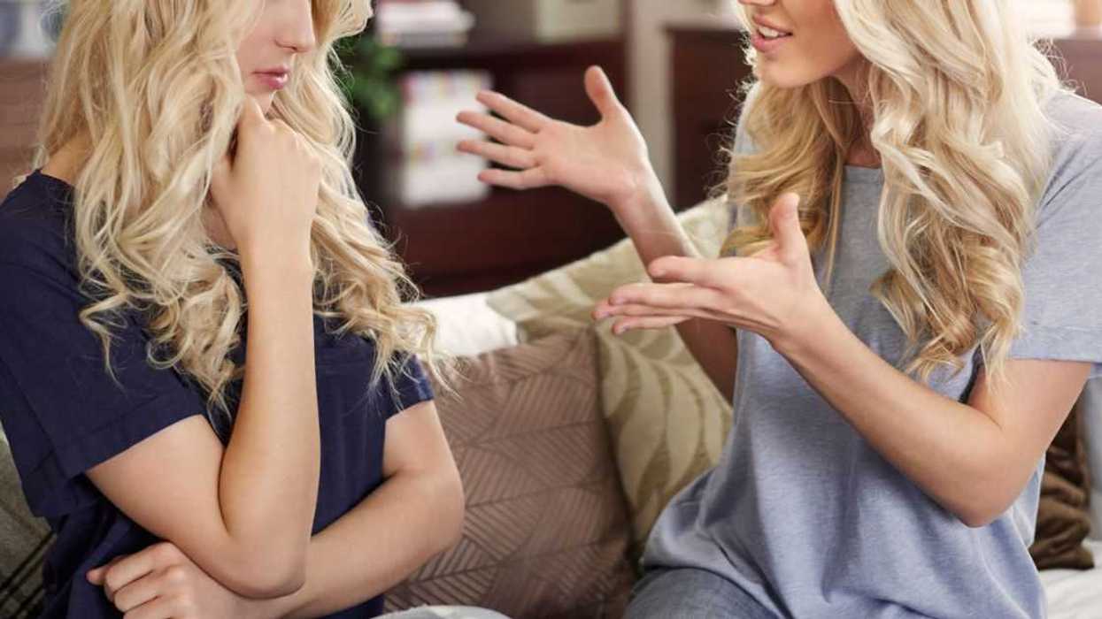 Blonde twin sisters sit on a couch and argue