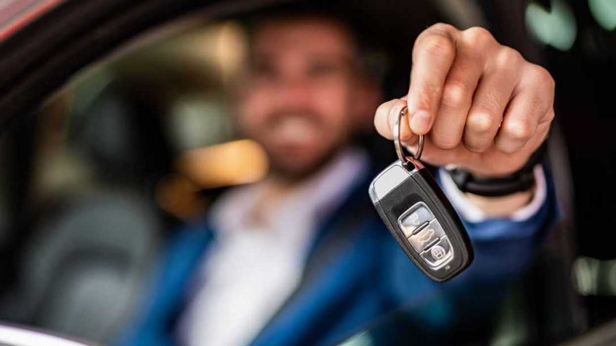 Blurry photo of adult man sitting in new car and showing car keys. Focus on foreground.