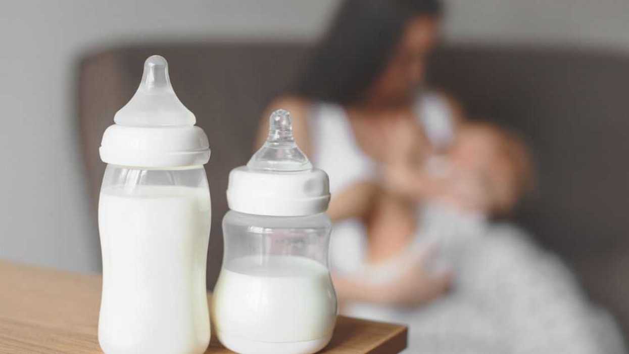 Bottles with breast milk on the background of mother holding in her hands and breastfeeding baby. Maternity and baby care.