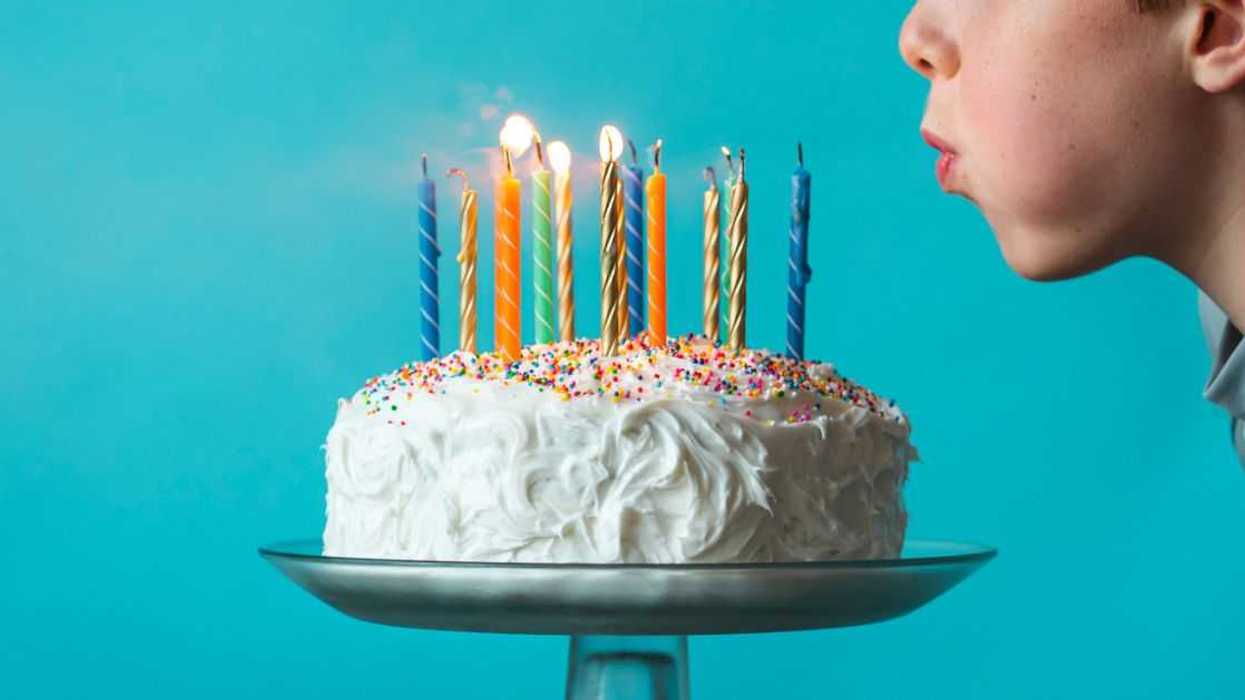 Boy blowing out candles on a birthday cake against blue background.