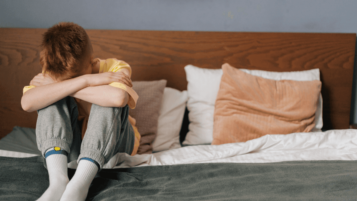 Boy sitting crouched down on a bed.