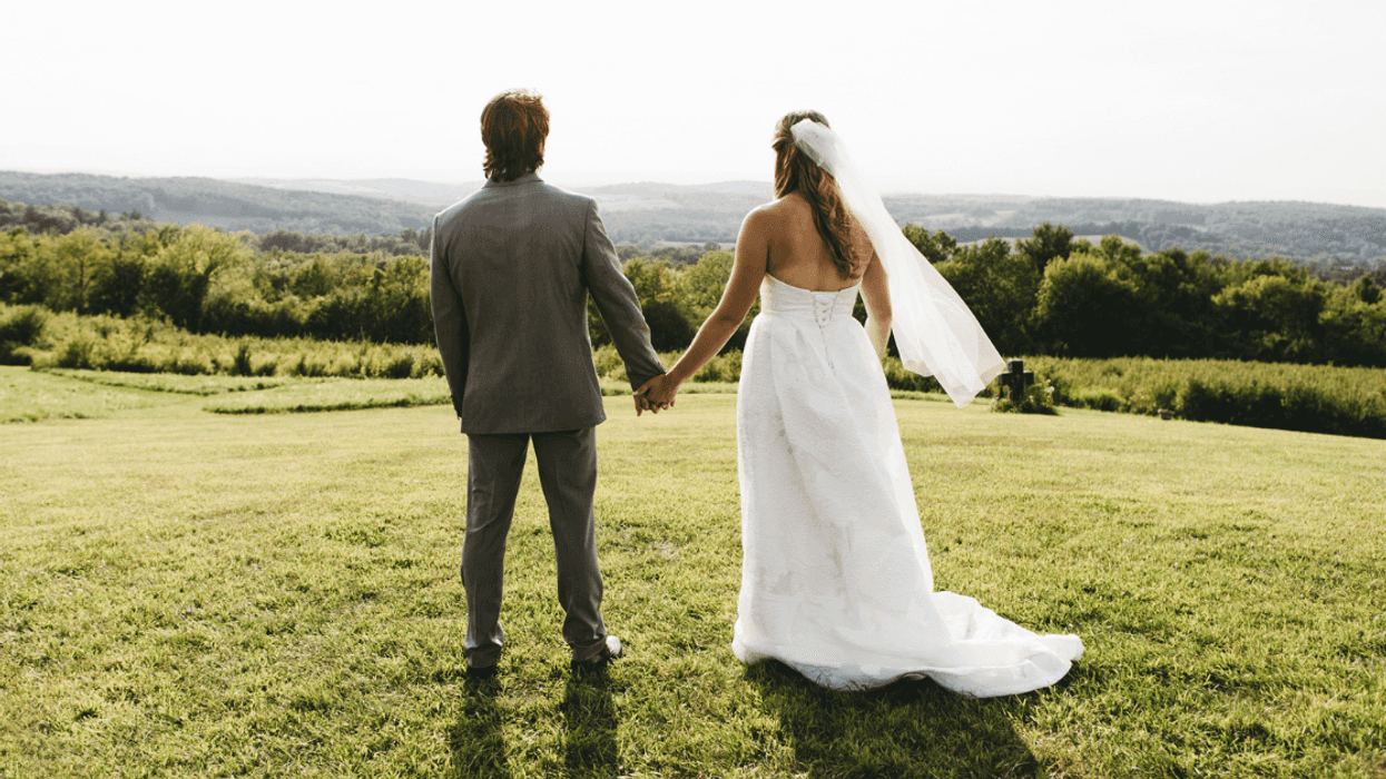 bride and groom holding hands on to of hill overlooking green valley