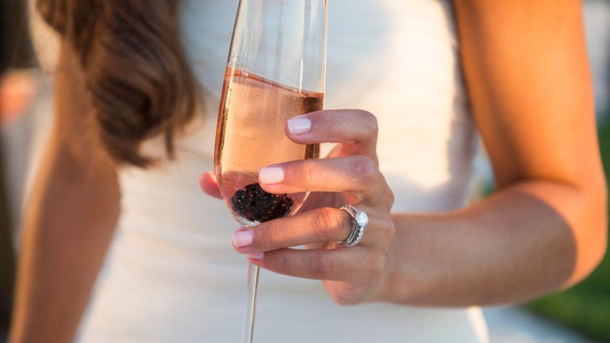 Bride holding blackberry rosé champagne in golden evening light.