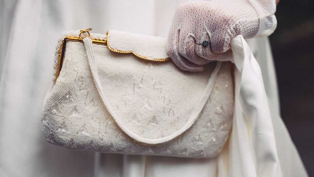 Bride holding white beaded purse bag. Pouch has gilded elements. Close-up.