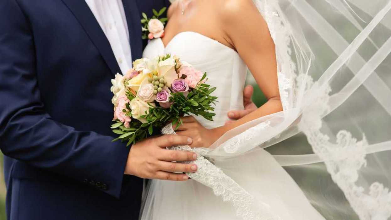 Bride in beautiful white wedding dress with bouquet and elegant groom in blue suit at happy wedding day.