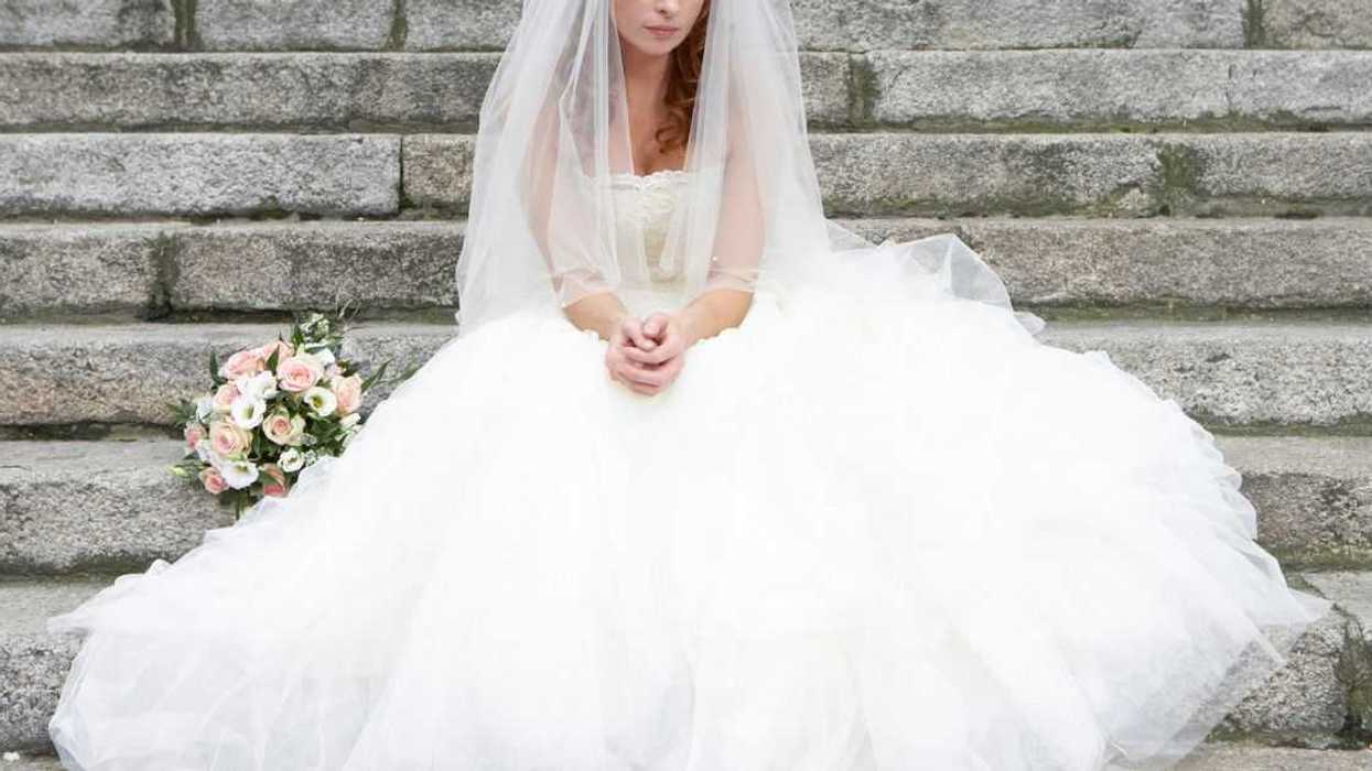 Bride sitting on stone steps, looking towards ground.