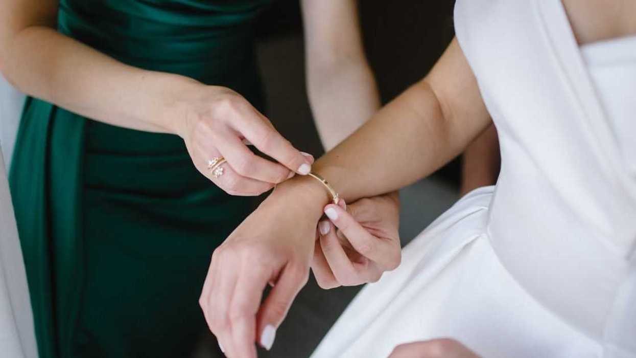 Bridesmaid in a dark green dress helps gorgeous bride to dress up and get ready for her wedding ceremony.