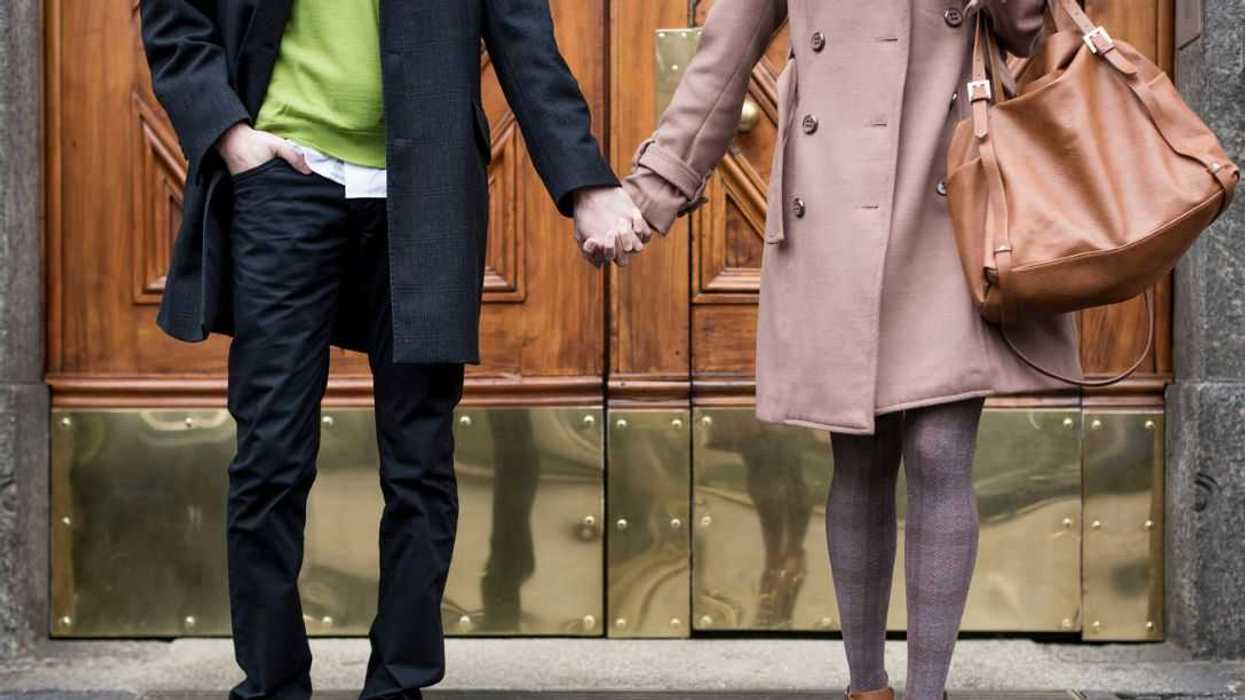 Businessman and businesswoman hand in hand in front of a gate.