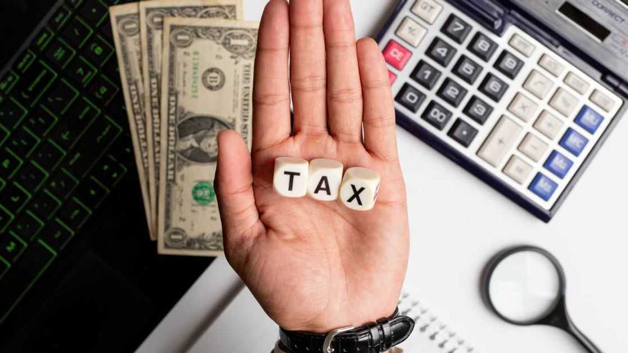Businessman making the word tax on wooden blocks on an office table with laptop, calculator, US dollars and diary on it.