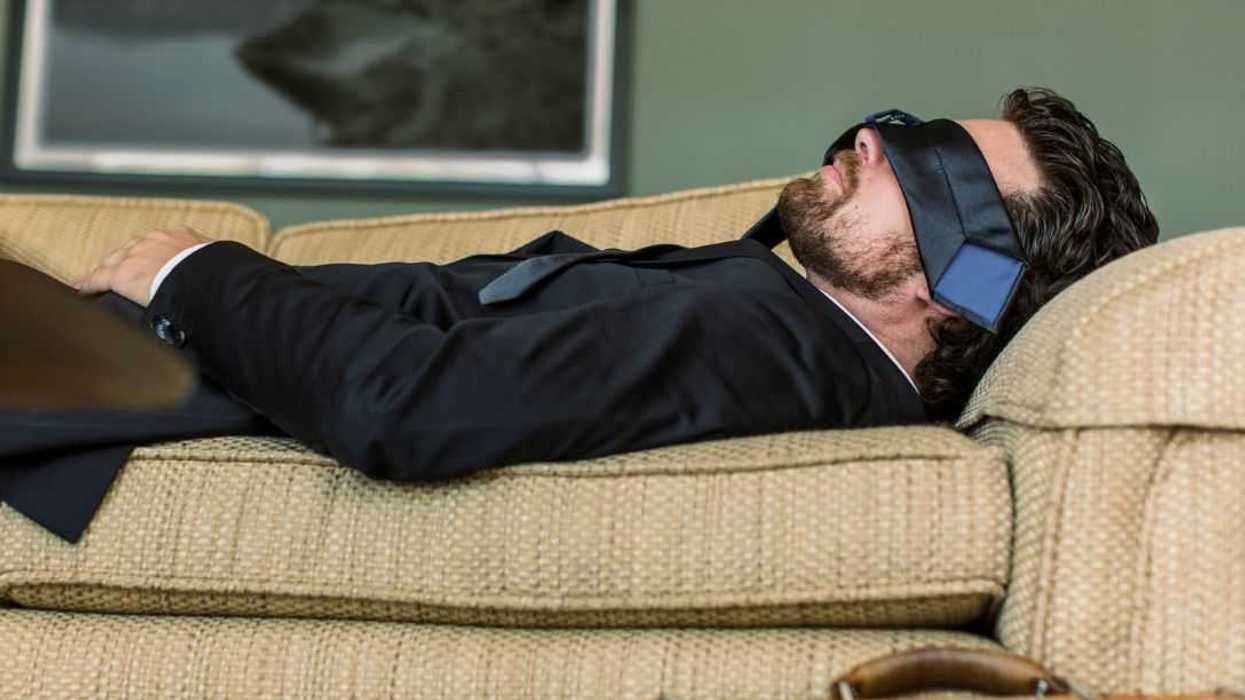 Businessman napping on sofa, tie over his eyes.