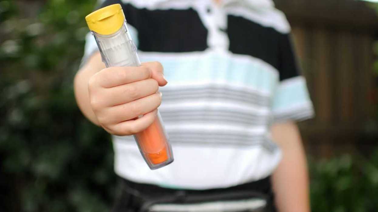 Child holding a anaphylaxis Auto injector with one also in small pouch. Carry case is being worn by a child.