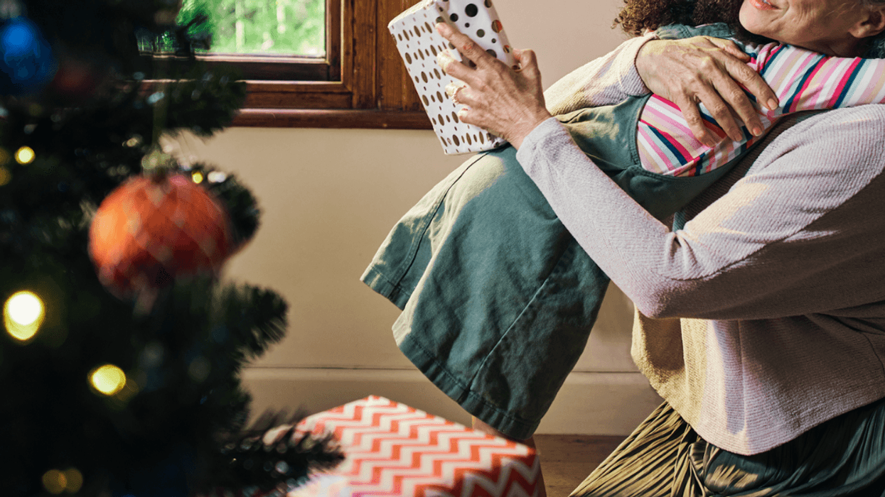 Child hugging her grandmother in front in front of a Christmas tree.
