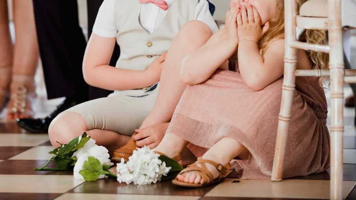 Children are sitting on the dancefloor by a table at a wedding.