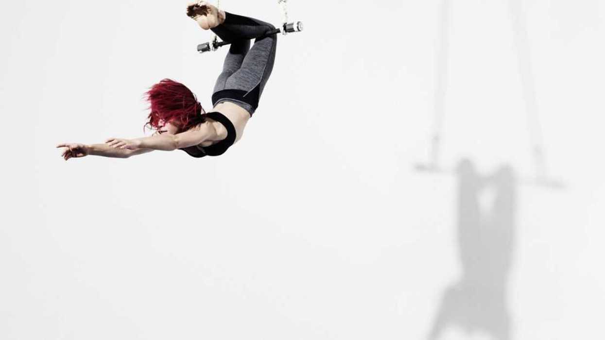 Circus artist in Trapeze, Photographed on white, with shadow projected on the wall