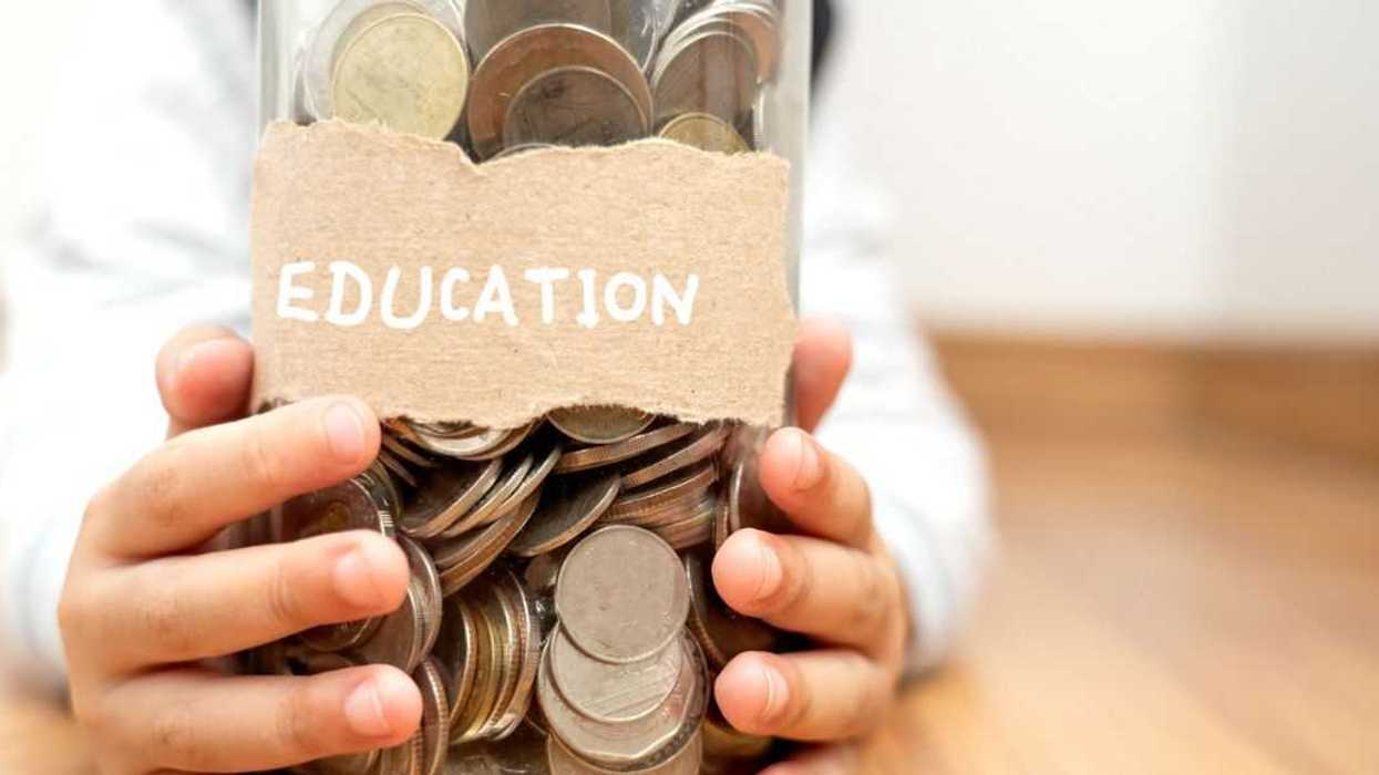 Close-up a young boy's ands holding a jar filler with coins. The jar is labeled "EDUCATION."