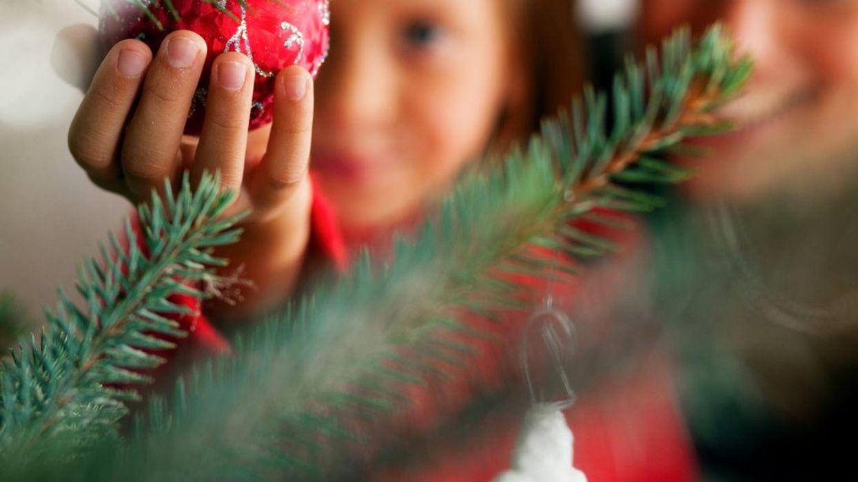 Close-up, blurred photo of a Mom holding up her daughter as she hangs an ornament on a Christmas tree.