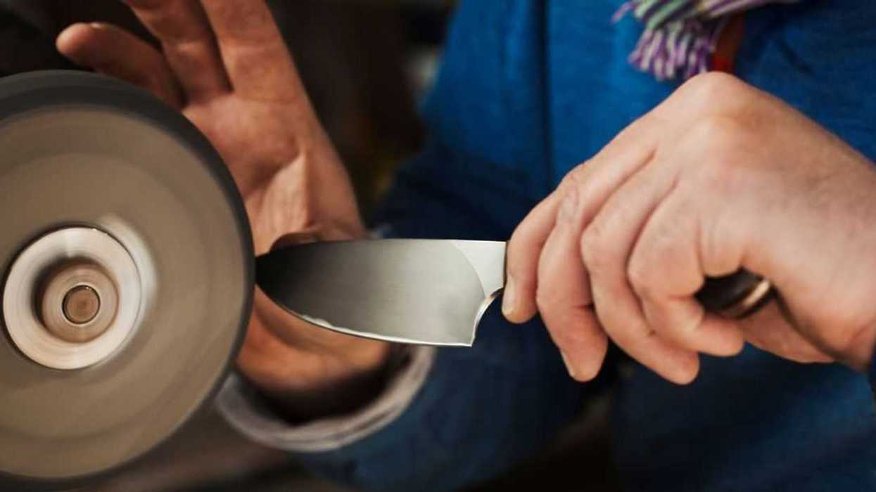 Close up of a craftsmans hands, holding a strong steel knife blade against a surface grinder, hand finishing a kitchen knife.
