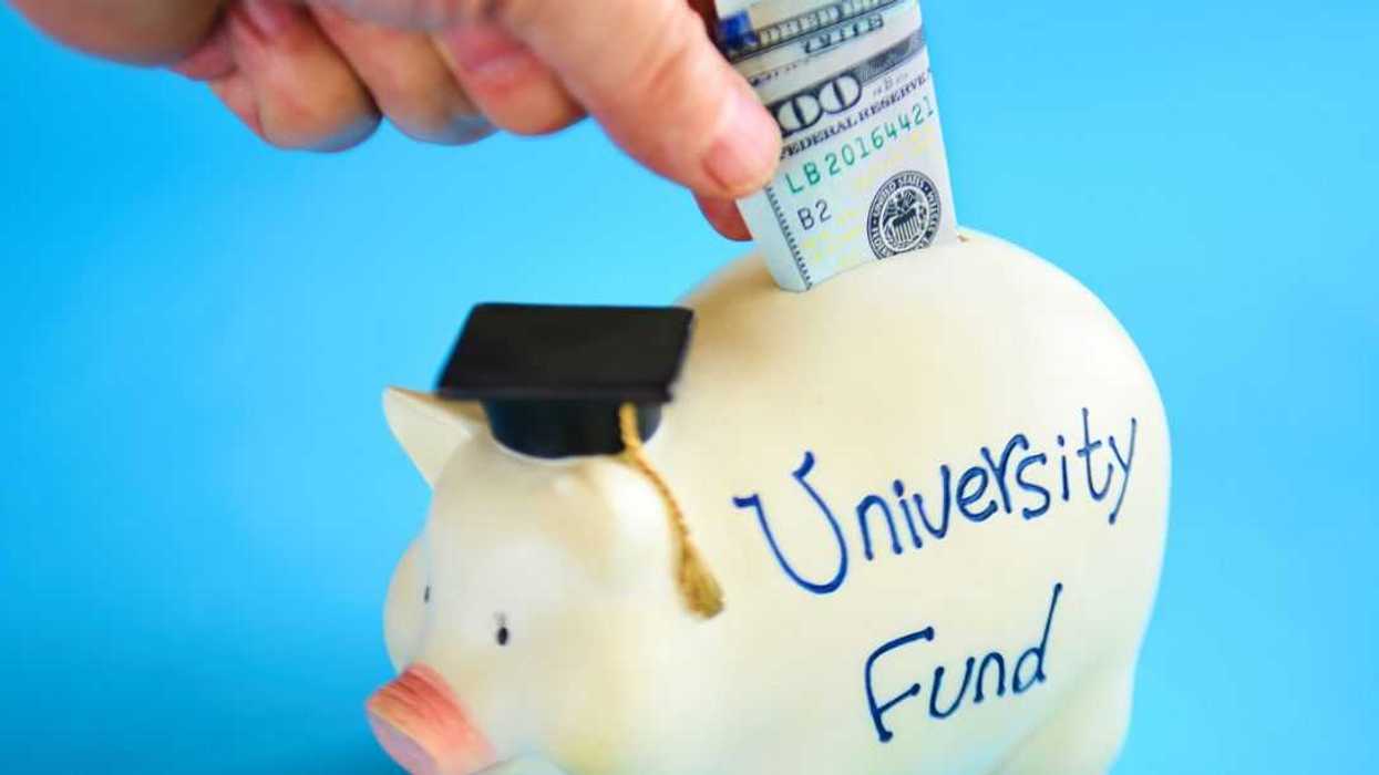 Close-up of a hand putting money into a piggy bank labeled, 'University Fund.'