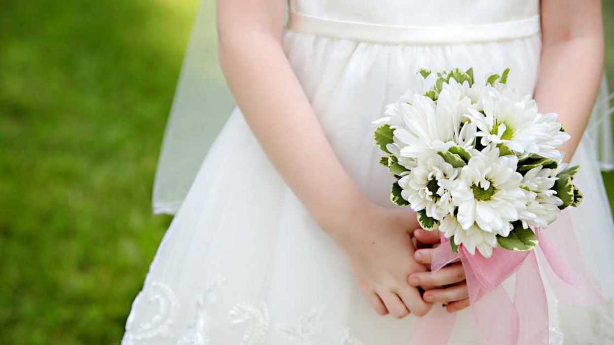 Close-up of a Little Girl in a First Communion or white Flower Girl Dress without her face, holding white and green flowers