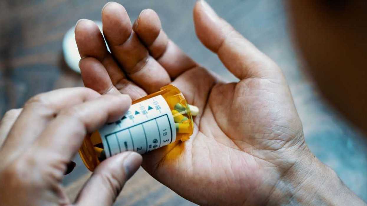 Close-up of a male hand holding, a pill bottle, pouring medication into his hand.
