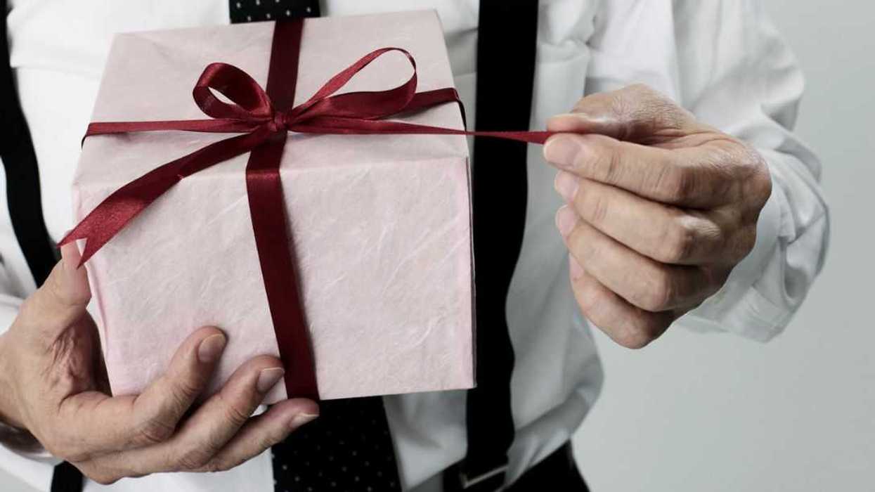 Close-up of a man's hands holding a gift box and pulling on it's string.
