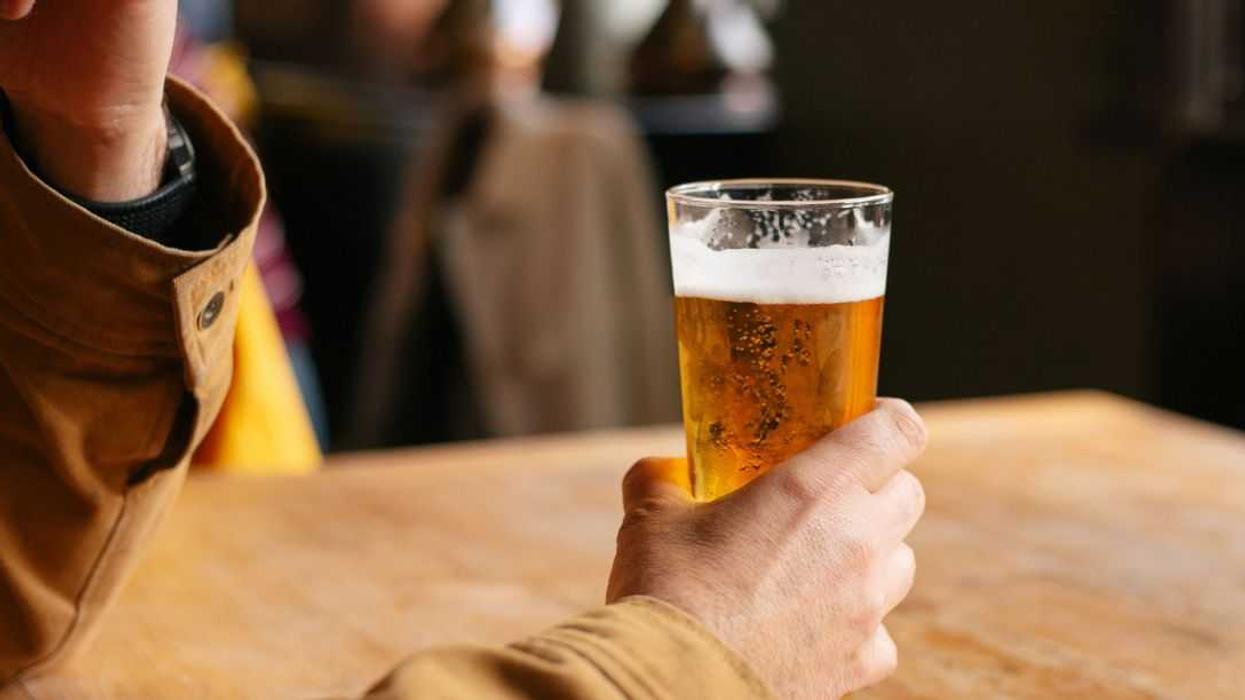 Close-up of a person holding a pint of beer at a wooden table in a pub.