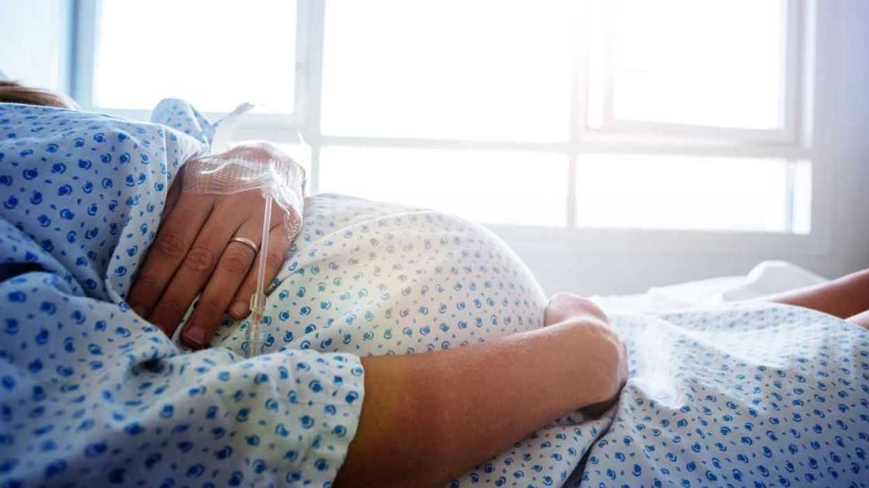 Close-up of a pregnant woman's belly in a hospital bed with a catheter in her hand