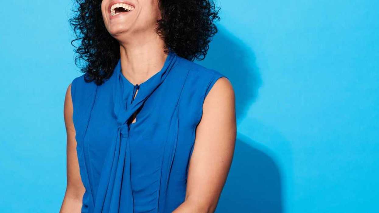 Close-up of a woman laughing and smiling against a blue background.