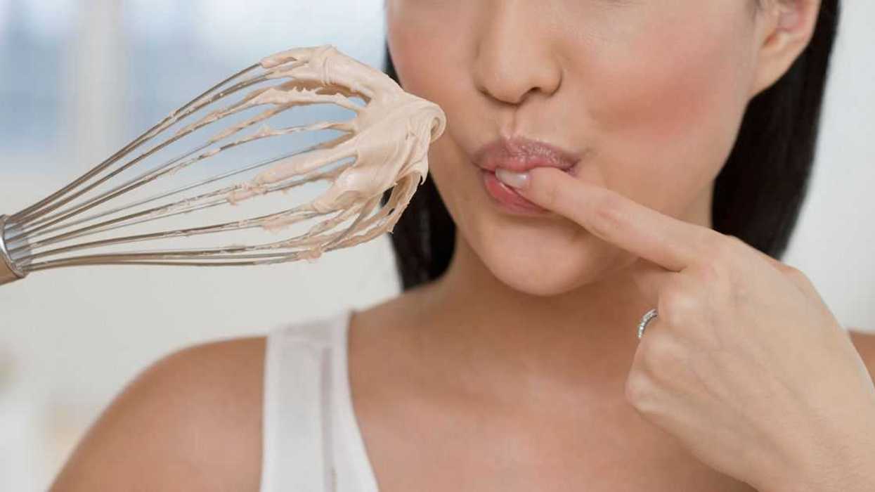 Close up of a woman tasting batter on a whisk.