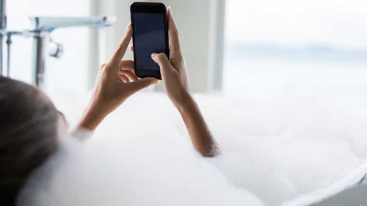 Close up of a woman using cell phone in bubble bath in a bathroom.