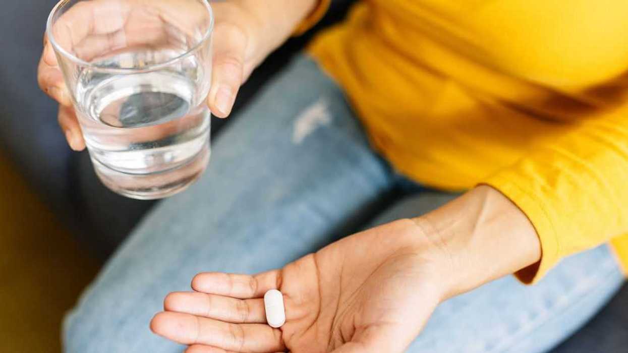 Close up of a young woman's hands, holding a white pill and a glass of water. Vitamins, pills and tablets. Health care and people concept.